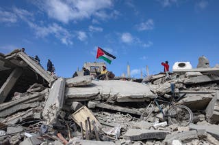 An internally displaced Palestinian waves a Palestinian flag over the rubble of a destroyed building amid a ceasefire between Israel and Hamas